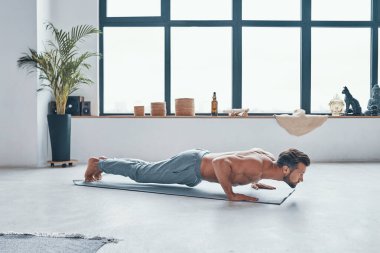 Yakışıklı genç adam evde egzersiz yaparken kalas pozisyonunu koruyor.