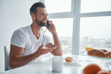 Mutfakta otururken telefonda konuşan yakışıklı genç adam.
