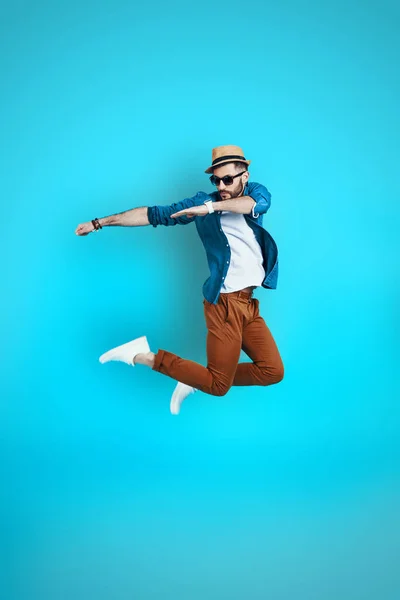 Full längd lekfull ung man dansar samtidigt svävar mot blå bakgrund — Stockfoto
