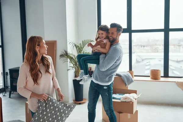 Παιχνιδιάρικη νεαρή οικογένεια χαμογελά και αποσυμπιέστε τα πράγματά τους, ενώ κινείται σε ένα νέο διαμέρισμα — Φωτογραφία Αρχείου