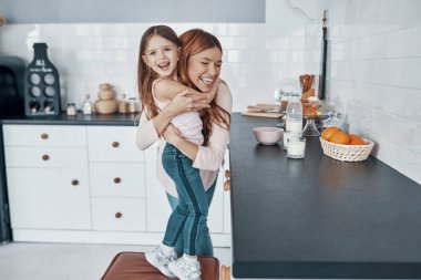 Genç ve güzel anne kızını kucaklıyor ve mutfakta bir şeyler hazırlarken gülümsüyor.