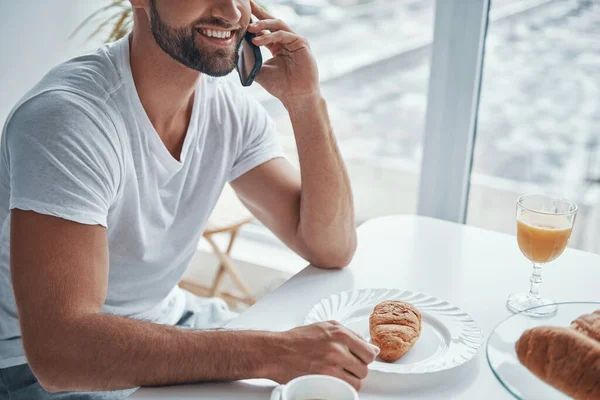 Primer plano de jóvenes guapos hablando por teléfono y sonriendo mientras están sentados en la cocina —  Fotos de Stock