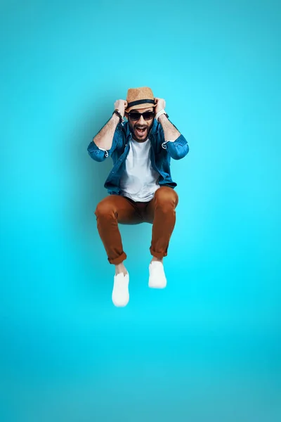 Full length of cheerful young man in casual wear smiling while standing against blue background — Stock Photo, Image