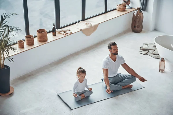 Vista dall'alto di padre e figlia che fanno yoga mentre sono seduti in posizione di loto a casa — Foto Stock