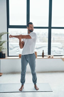 Tam boy yakışıklı genç adam evde halıda dururken spor yapıyor.