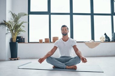 Evde lotus pozisyonunda otururken yoga yapan yakışıklı genç adam.