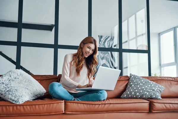 Приваблива молода жінка використовує ноутбук і посміхається, проводячи час вдома — стокове фото