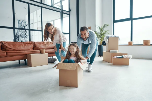 Χαρούμενη νεαρή οικογένεια χαμογελά και αποσυμπιέστε τα πράγματά τους, ενώ κινείται σε ένα νέο διαμέρισμα — Φωτογραφία Αρχείου