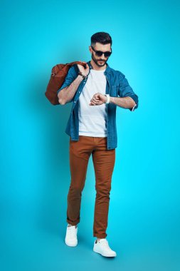 Tam boy yakışıklı genç adam kahverengi arka planda yürürken saati kontrol ediyor.