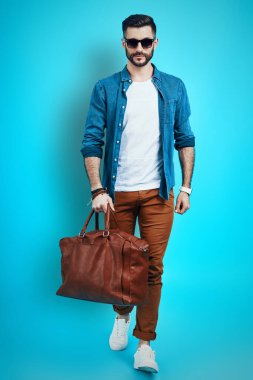 Mavi arka planda yürürken gülümseyen ve kameraya bakan zarif bir genç.