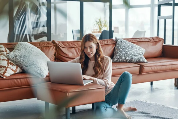 Piękna młoda kobieta korzystająca z laptopa i uśmiechnięta podczas spędzania czasu w domu — Zdjęcie stockowe