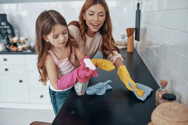 Madre e hija limpiando el polvo usando guantes de lavar mientras pasan tiempo en casa —  Fotos de Stock