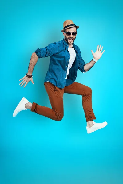 Full length of playful young man smiling and gesturing while hovering against blue background — Stock Photo, Image