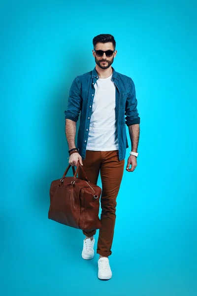 Full length of fashionable young man smiling and looking at camera while walking against blue background — Stock Photo, Image