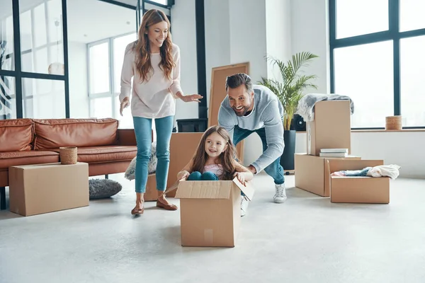 Παιχνιδιάρικη νεαρή οικογένεια χαμογελά και αποσυμπιέστε τα πράγματά τους, ενώ κινείται σε ένα νέο διαμέρισμα — Φωτογραφία Αρχείου