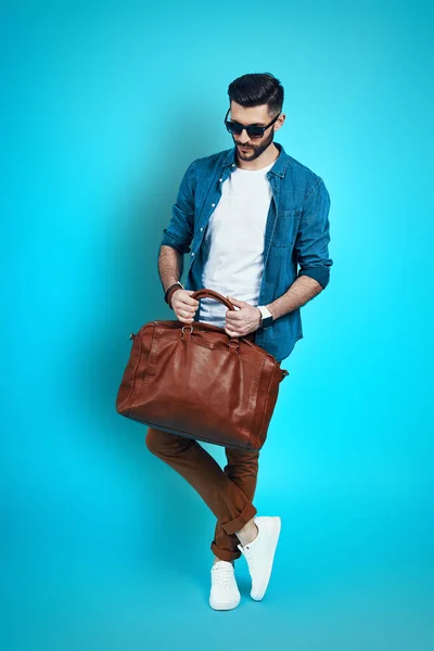 Plná délka pohledný stylový mladý muž přizpůsobení taška, zatímco stojí na modrém pozadí — Stock fotografie