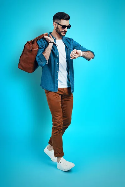 Pleine longueur de jeune homme à la mode souriant et vérifiant l'heure tout en marchant sur fond brun — Photo