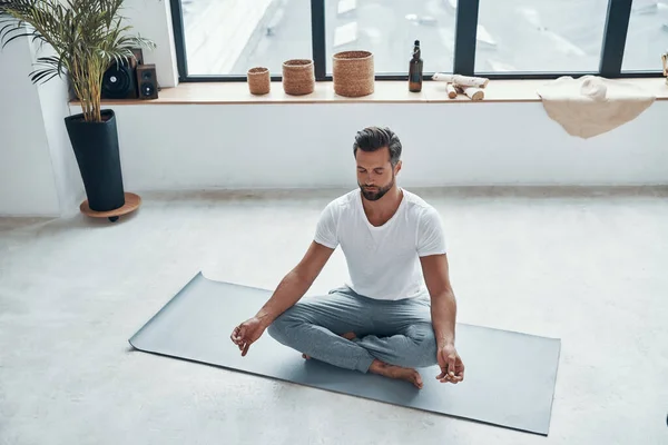 Vista dall'alto del bel giovane che fa yoga mentre è seduto in posizione di loto a casa — Foto Stock