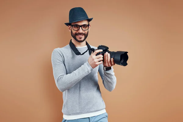 Beau jeune homme en tenue décontractée regardant la caméra et souriant tout en se tenant debout sur fond brun — Photo