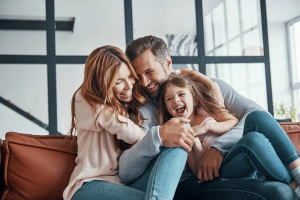 Feliz familia joven sonriendo y abrazando mientras se unen en casa —  Fotos de Stock