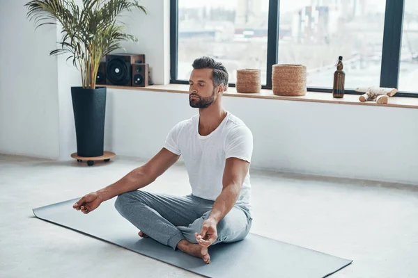 Totalmente rilassato giovane uomo che fa yoga mentre seduto in posizione loto a casa — Foto Stock