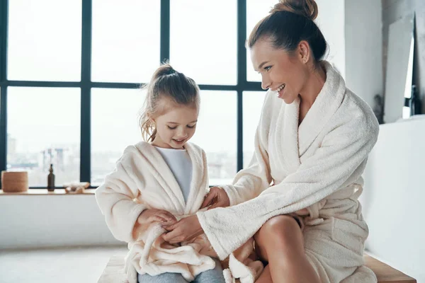 Mor med dotter i badrockar ler medan du gör morgon rutin — Stockfoto