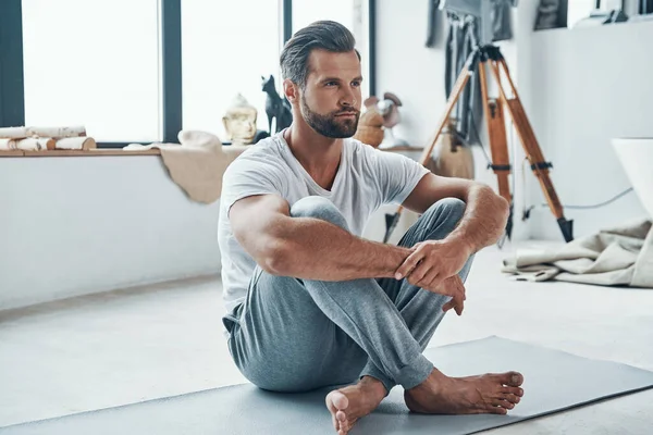 Bello giovane uomo tenere insieme le gambe mentre fa fitness a casa — Foto Stock