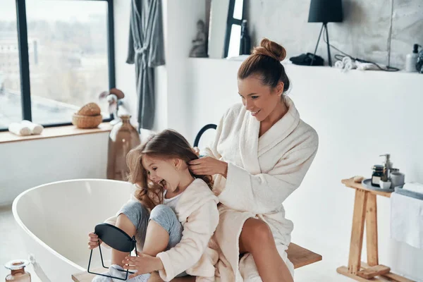 Beautiful young mother combining her daughters hair while doing morning routine — Stock Photo, Image