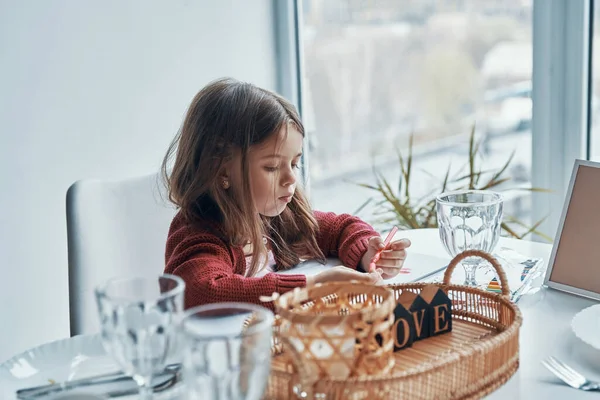 Petite fille mignonne peignant quelque chose tout en étant assis dans la cuisine à la maison — Photo