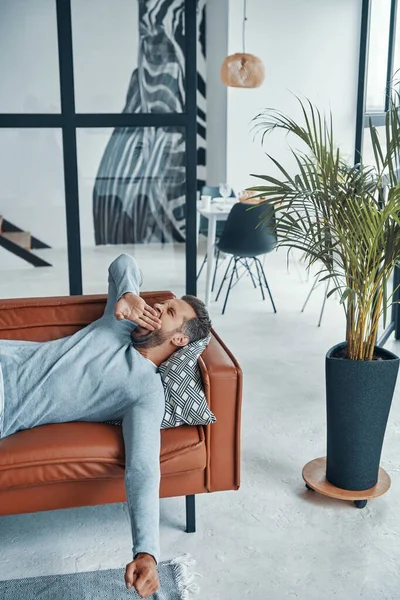Stilig ung man i avslappnade kläder gäspande medan liggande på soffan hemma — Stockfoto