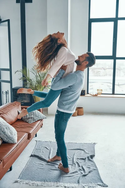 Longitud completa de la joven pareja juguetona sonriendo y bailando mientras se unen en casa — Foto de Stock