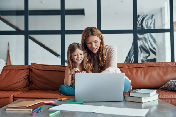 Η νεαρή όμορφη μητέρα και η κορούλα της ενώνονται και χαμογελούν ενώ χρησιμοποιούν φορητό υπολογιστή στο σπίτι — Φωτογραφία Αρχείου