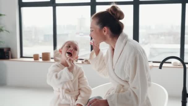 Mutter und Tochter in Bademänteln lächeln und Zähne putzen — Stockvideo