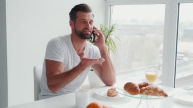 Mutfakta kahvaltı ederken telefonda konuşan yakışıklı genç adam.