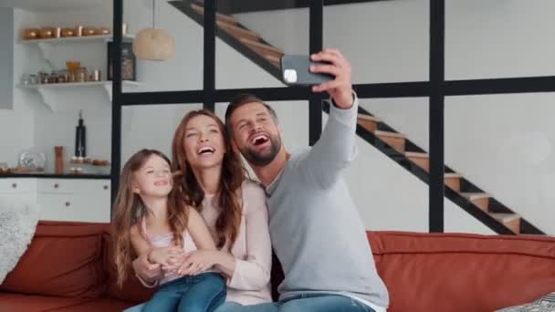 Χαρούμενη νεαρή οικογένεια χαμογελά και αγκαλιάζει, ενώ κάνει selfie στο σπίτι μαζί — Αρχείο Βίντεο