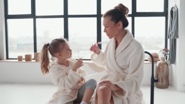 Lekfull mamma och dotter i badrockar ler och rengör tänderna — Stockvideo