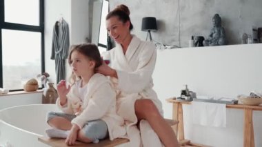 Mutlu genç anne sabah rutinini yaparken kızının saçını birleştiriyor.