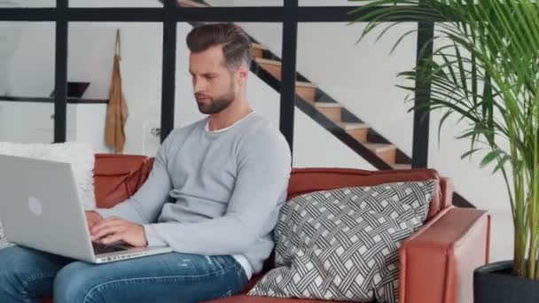 Ung man ser trött efter jobbet hemma medan du sitter på soffan — Stockvideo
