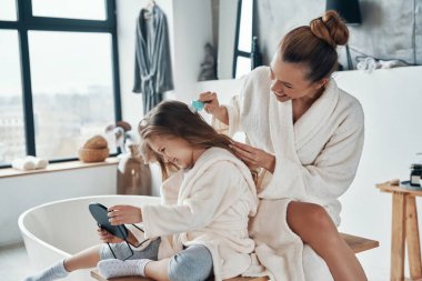 Güzel genç anne sabah rutinini yaparken kızının saçını birleştiriyor.