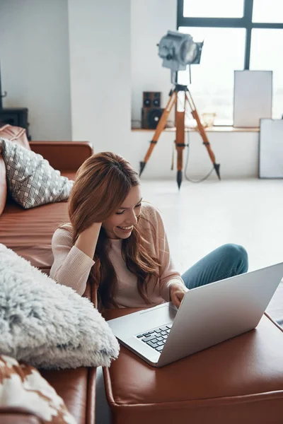 Привлекательная молодая женщина использует ноутбук и улыбается, проводя время дома — стоковое фото
