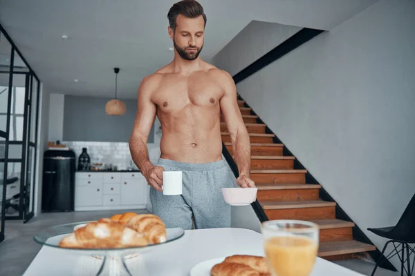 Hombre joven de buen aspecto desayunando mientras pasa tiempo en la cocina casera —  Fotos de Stock