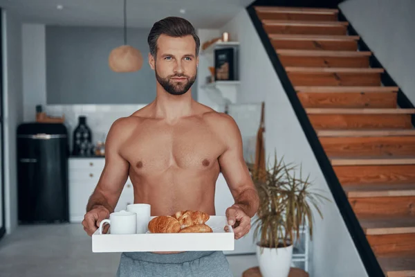 Joven guapo sosteniendo bandeja con desayuno mientras pasa tiempo en casa —  Fotos de Stock