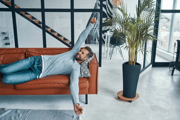 Handsome young man in casual clothing stretching and smiling while lying — Stock Photo, Image