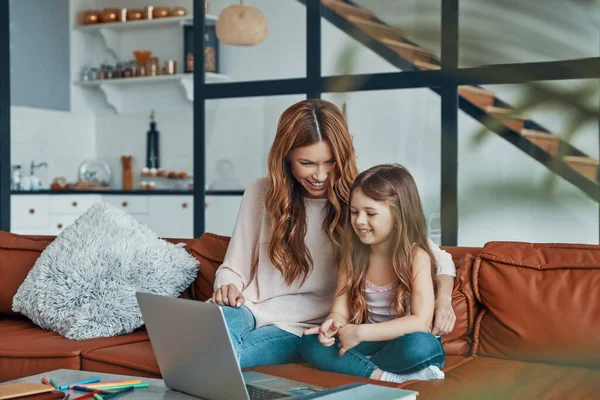 Moeder en haar dochter hechting samen en glimlachen tijdens het gebruik van laptop thuis — Stockfoto