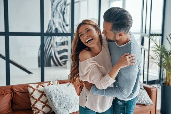 Joyeux jeune couple souriant et embrassant tout en collant ensemble à la maison — Photo