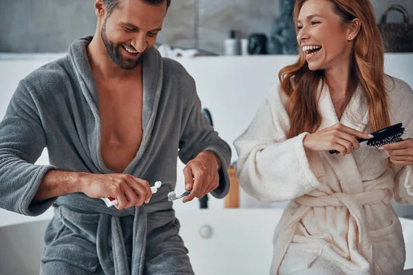 Älskade unga par i badrockar skrattar medan du gör morgon rutin — Stockfoto