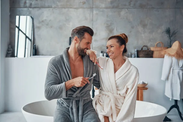 Mooi jong paar in badjassen schoonmaken tanden terwijl het doen van ochtend routine — Stockfoto