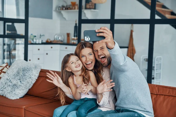 Juguetón joven familia sonriendo y utilizando el teléfono inteligente para tomar una selfie —  Fotos de Stock