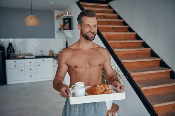 Bel giovane uomo che tiene il vassoio con la colazione mentre trascorre del tempo a casa — Foto Stock