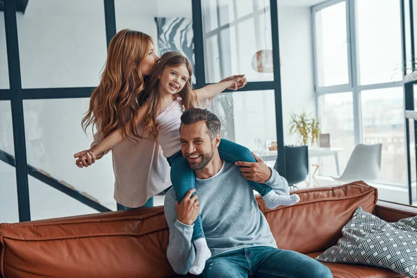 Hermosa familia joven sonriendo y abrazando mientras se unen en casa —  Fotos de Stock